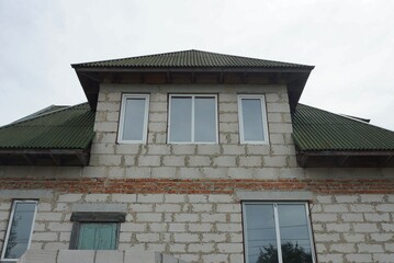 Obraz premium facade of a gray private brick house with windows under a green tiled roof against the sky
