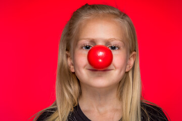 Little Girl Wearing a Red Clown Nose Against a Red Background
