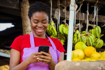 a young beautiful african market woman feeling happy about what she saw on her cellphone