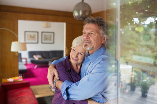 Happy senior couple hugging at sunny living room window