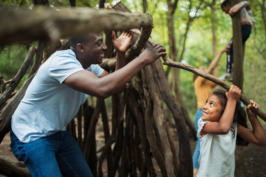 Father and daughter building teepee with branches in woods
