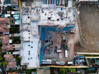 A building under construction with fifteen floors looked from above to the rooftop with a drone in the middle of an urban neighborhood 
