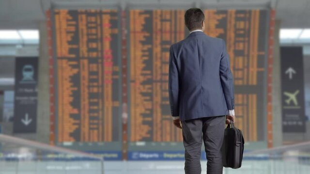businessman hold a laptop bag stand and look at airport timetable schedule, life after self isolation