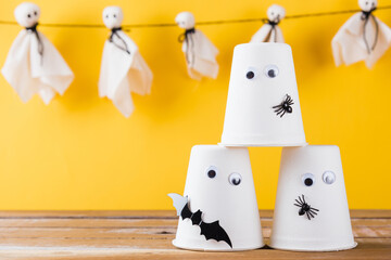 Funny Halloween day decoration party, Baby cute white ghost crafts scary face hanging and halloween crafts paper cup ghost on wood, studio shot isolated, Happy holiday DIY handicraft concept