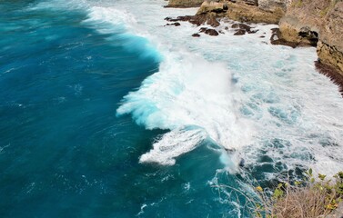 Waves crashing on rocks in blue ocean water in Nusa Penida, Indonesia