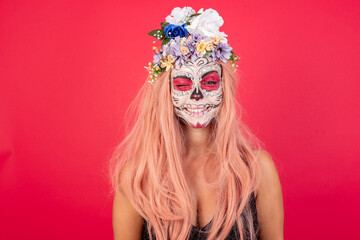 young beautiful woman wearing halloween make up over red background blinking one eye and smiling.