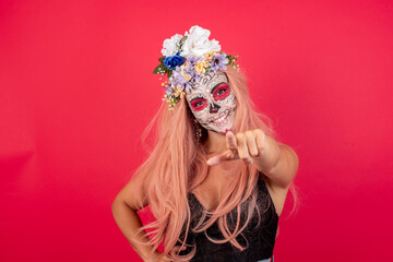 young beautiful woman wearing halloween make up over red background pointing at camera with a satisfied, confident, friendly smile, choosing you