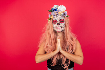 young beautiful woman wearing halloween make up over red background praying with hands together asking for forgiveness smiling confident.