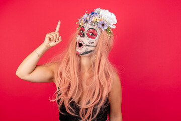 young beautiful woman wearing halloween make up over red background pointing finger up with successful idea. Exited and happy. Number one.