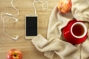 Phone mockup, sweater, cup of hot tea and apples on the wooden background. Cozy autumn or winter consept.