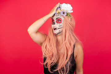 young beautiful woman wearing halloween make up over red studio surprised with hand on head for mistake, remember error. Forgot, bad memory concept.
