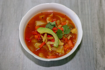 A bowl of chicken tortilla soup topped with crispy tortilla strips, avocado and cilantro.