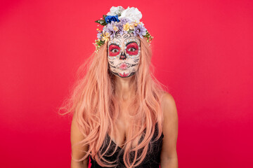 Shot of pleasant looking young beautiful woman wearing halloween make up over red background, pouts lips, looks with green eyes at camera,  has fun with girlfriend, Human facial expressions