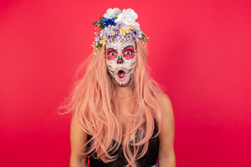 Oh my God. Surprised young beautiful woman wearing halloween make up over red background stares at camera with shocked expression exclaims with unexpectedness,