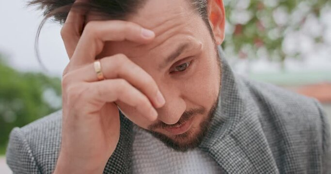 Close up of young mans' face with mustaches and a beard. Worried, he touches his mouth with his hand, then his forehead and again thoughtfully covers his mouth with hand, looking straight to the