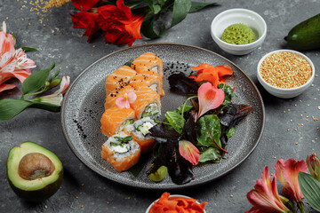 Delicious fresh sushi rolls with salmon and philadelphia cheese on gray plate on dark stone background. Traditional japanese seafood, healthy food concept
