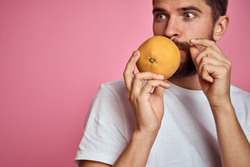 Young man with orange on a pink background in a white t-shirt emotions fun gesticulating with model hands