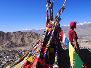 A woman with a bright blue sky and a colorful Talcho (Tibetan praying flags), Namgyal Tsemo Gompa, Leh, Ladakh, Jammu and Kashmir, India