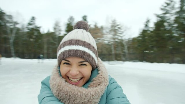 Portrait of happy young woman in warm clothes ice-skating laughing having fun looking at camera in park in winter. Recreational activities and youth concept.