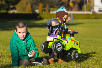 Two cheerful brothers-boys of different ages have fun playing with a big jeep in a wheelchair on a green field on a warm summer day. Brothers friendship and happy childhood concept.