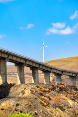 Highway overpass crossing a valley. On the hill there is a wind turbine for the production of wind energy.