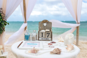 Close up view of table for the beach wedding ceremony with decoration of shells, jars with color sand, wooden calendar inside bamboo gazebo, Punta Cana, Dominican Republic