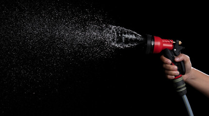 Hand hold a gun watering hose with water splash against on black background,spraying hose nozzle