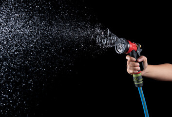  Hand hold a gun watering hose with water splash against on black background,spraying hose nozzle