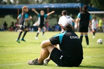 Staff coaches who sitting to watch athletes compete on the side of the field. Rear view.