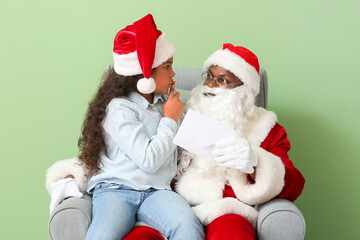 African-American Santa Claus and cute little girl with letter on color background