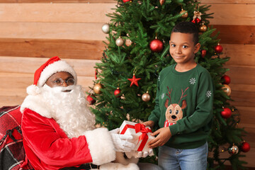 Fototapeta na wymiar African-American Santa Claus giving present to cute little boy at home