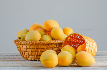 Apricots in wicker baskets on wooden and white gradient background. side view.