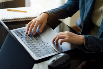 Business woman hands typing on laptop computer keyboard with notebook and pen on the desk at modern home office. 