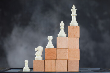 Business hierarchy concept with figures on pyramid of wooden blocks on foggy and chessboard...
