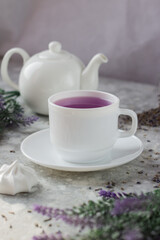 Obraz na płótnie Canvas lavender tea in a white mug. Purple tea in a mug on a light background stands on the table next to lavender flowers. Dried lavender flowers are brewed in a Cup.