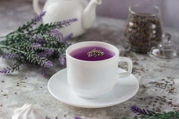 lavender tea in a white mug. Purple tea in a mug on a light background stands on the table next to lavender flowers. Dried lavender flowers are brewed in a Cup.