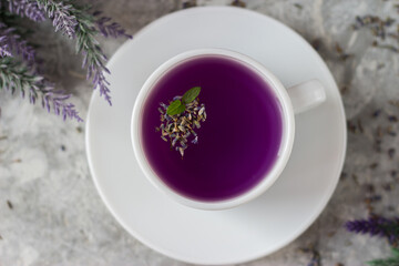 lavender tea in a white mug. Purple tea in a mug on a light background stands on the table next to lavender flowers. Dried lavender flowers are brewed in a Cup.
