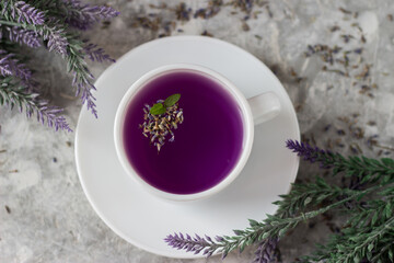 lavender tea in a white mug. Purple tea in a mug on a light background stands on the table next to lavender flowers. Dried lavender flowers are brewed in a Cup.