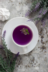 lavender tea in a white mug. Purple tea in a mug on a light background stands on the table next to lavender flowers. Dried lavender flowers are brewed in a Cup.