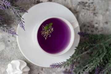 lavender tea in a white mug. Purple tea in a mug on a light background stands on the table next to lavender flowers. Dried lavender flowers are brewed in a Cup.