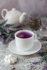 lavender tea in a white mug. Purple tea in a mug on a light background stands on the table next to lavender flowers. Dried lavender flowers are brewed in a Cup.