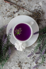 lavender tea in a white mug. Purple tea in a mug on a light background stands on the table next to lavender flowers. Dried lavender flowers are brewed in a Cup.