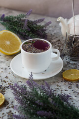 lavender tea in a white mug. Purple tea in a mug on a light background stands on the table next to lavender flowers. Dried lavender flowers are brewed in a Cup.