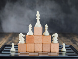 Business hierarchy concept with chessboard, figures on pyramid of wooden blocks on foggy and wooden...