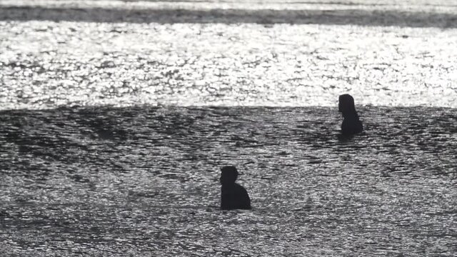 Surfers waiting patiently in lineup for next wave, bright sunlight on surface