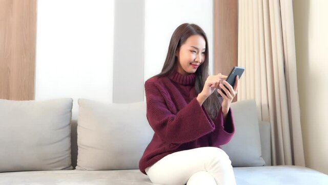 Young Pretty Asian Woman Texting and Chatting on Smartphone at Living Room Sofa. Modern Netwroking and Communication Concept, Full Frame Slow Motion