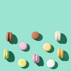 Pattern from different cake macaroons on bright blue green color background, multi colored french biscuit macarons.