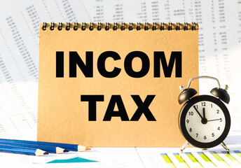 Notebook, pencils and clocks on the table with financial papers. your text INCOM TAX