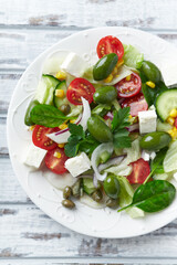 Healthy Salad with Feta Cheese, Green Olives, Baby Spinach, Cucumber, Cherry Tomatoes and Capers. Bright wooden background. Top view. Close up. 