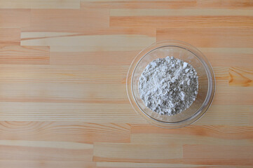 Raw eggs and flour in glass bowls are on the wooden board in the kitchen.